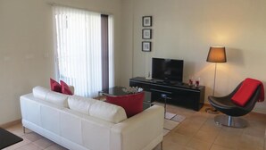 Un salón con un sofá blanco, un mueble de entretenimiento negro, una butaca roja y una lámpara de pie.