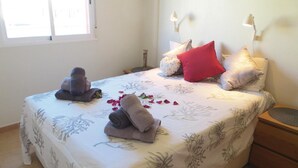 Una cama bien hecha con toallas, un almohadón rojo y una lámpara de noche.
