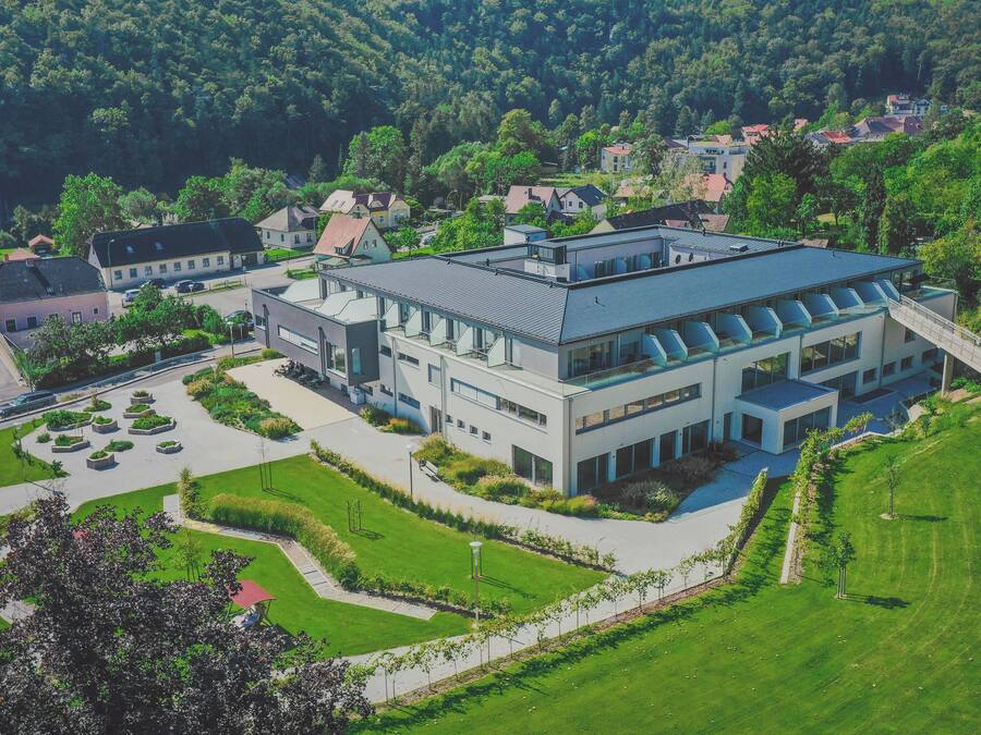 Un bâtiment moderne doté d’un toit plat, entouré de pelouses verdoyantes et d’arbres.
