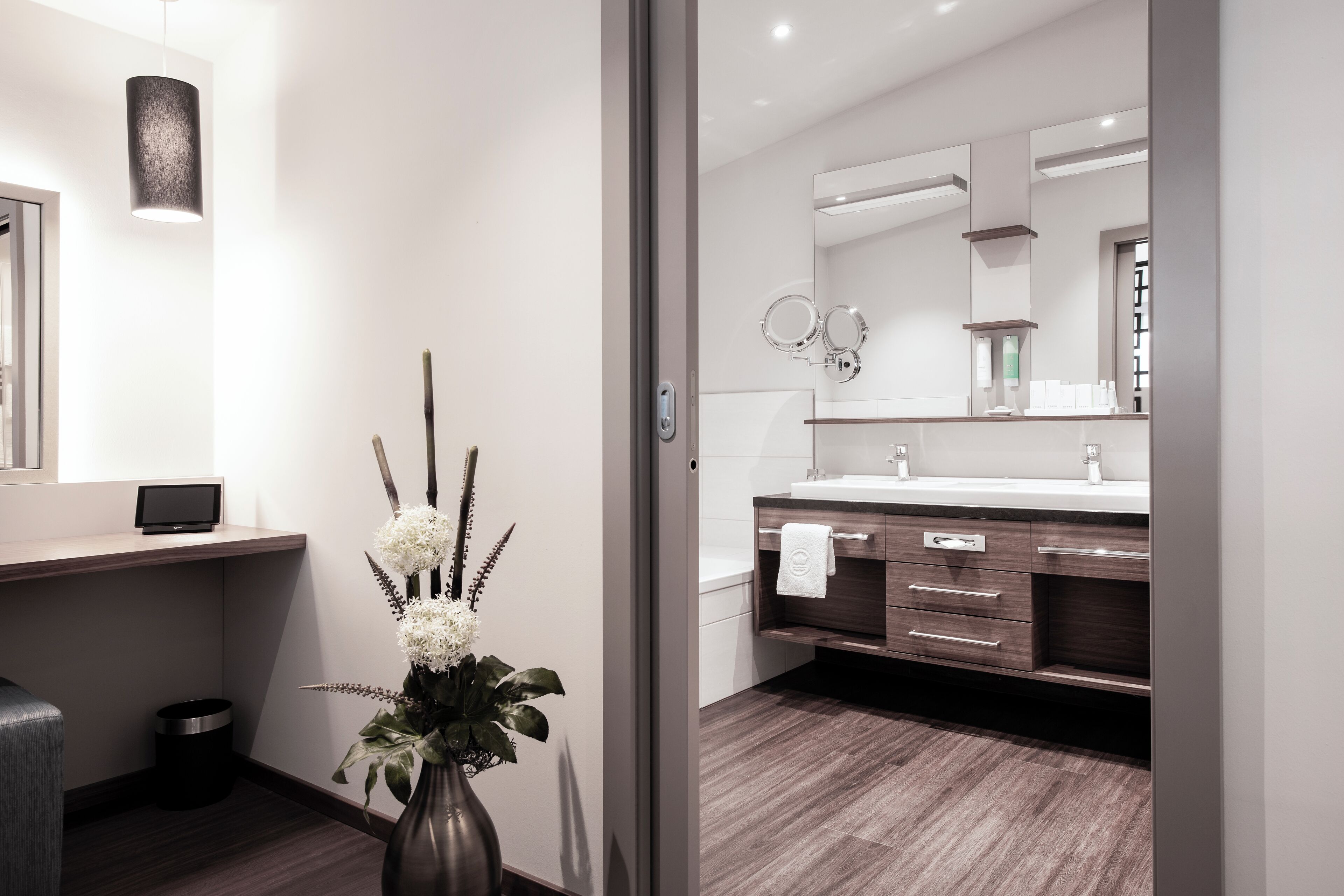 A modern bathroom with a large mirror, wooden vanity, and a vase of flowers.