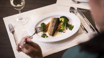 A dining table with a plate of food, a fork, and a glass of wine.