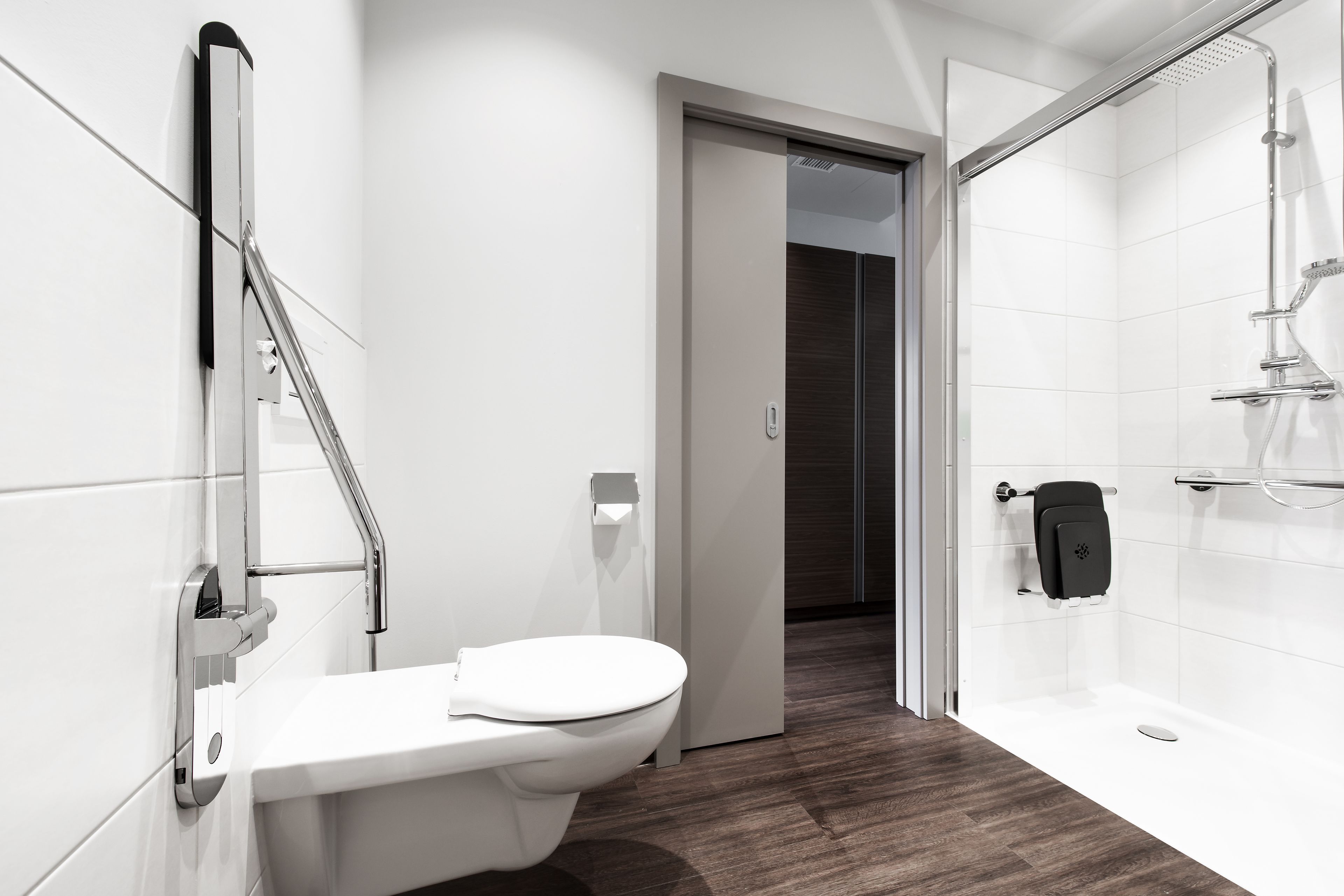 A modern bathroom with a toilet, a shower, and a glass door leading to another room.