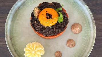 Plat rodó de ceràmica amb un centre de postre, decorat amb una fulla verda i una flor groga, damunt una superfície de fusta fosca.