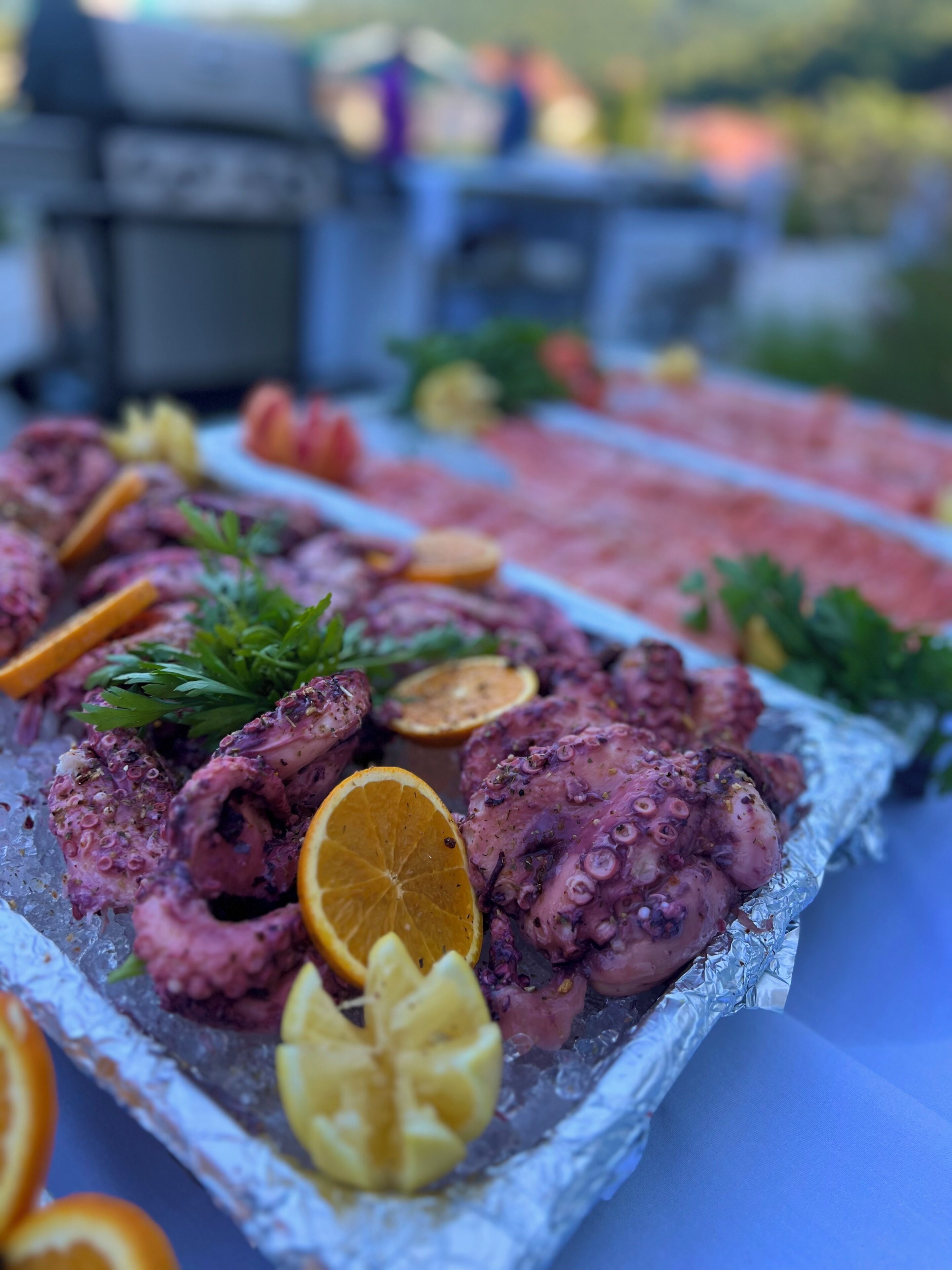 Una bandeja de mariscos con pulpo y adornos cítricos sobre hielo, colocada al aire libre.