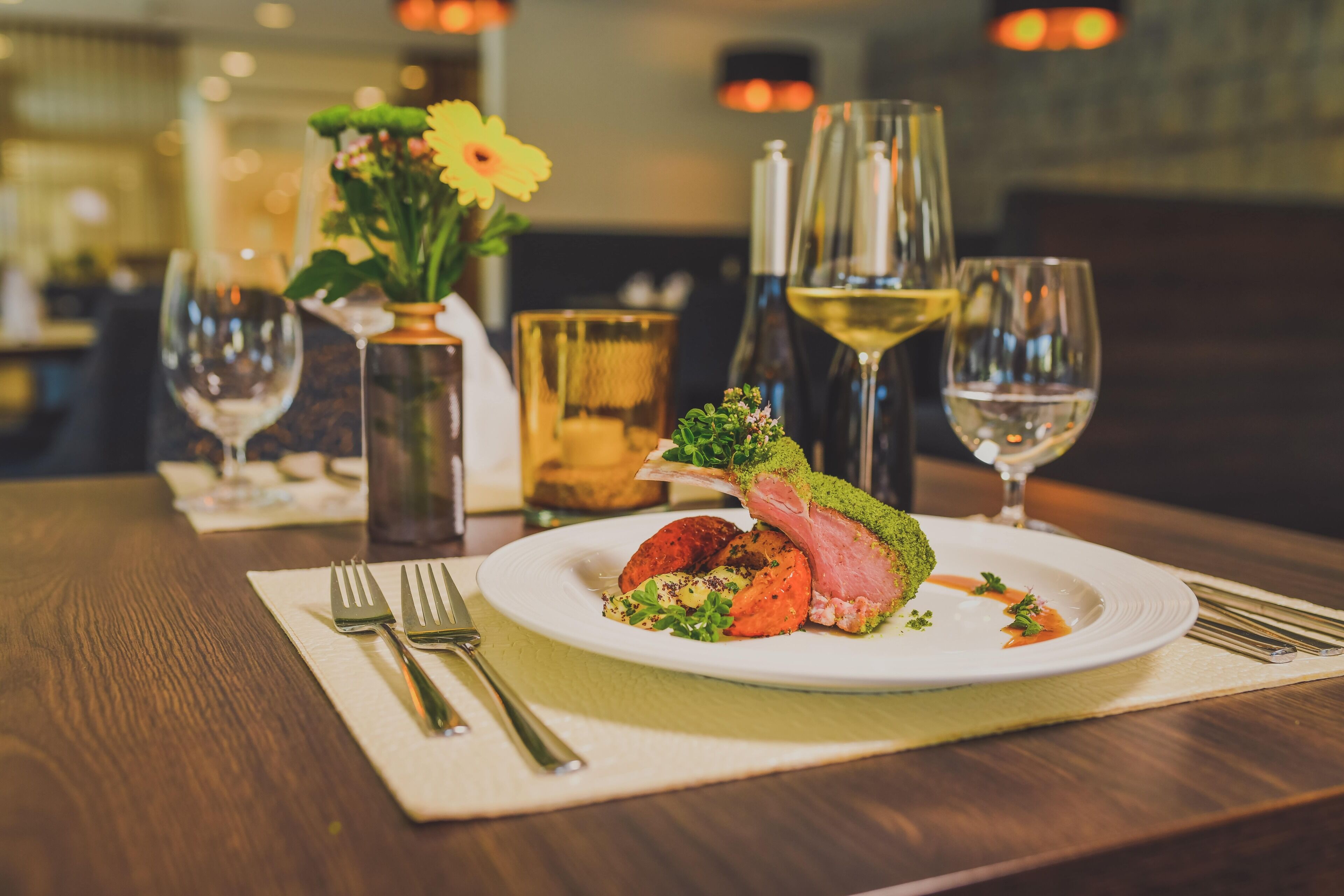 A dining table with a plate of food, a vase with flowers, and wine glasses.