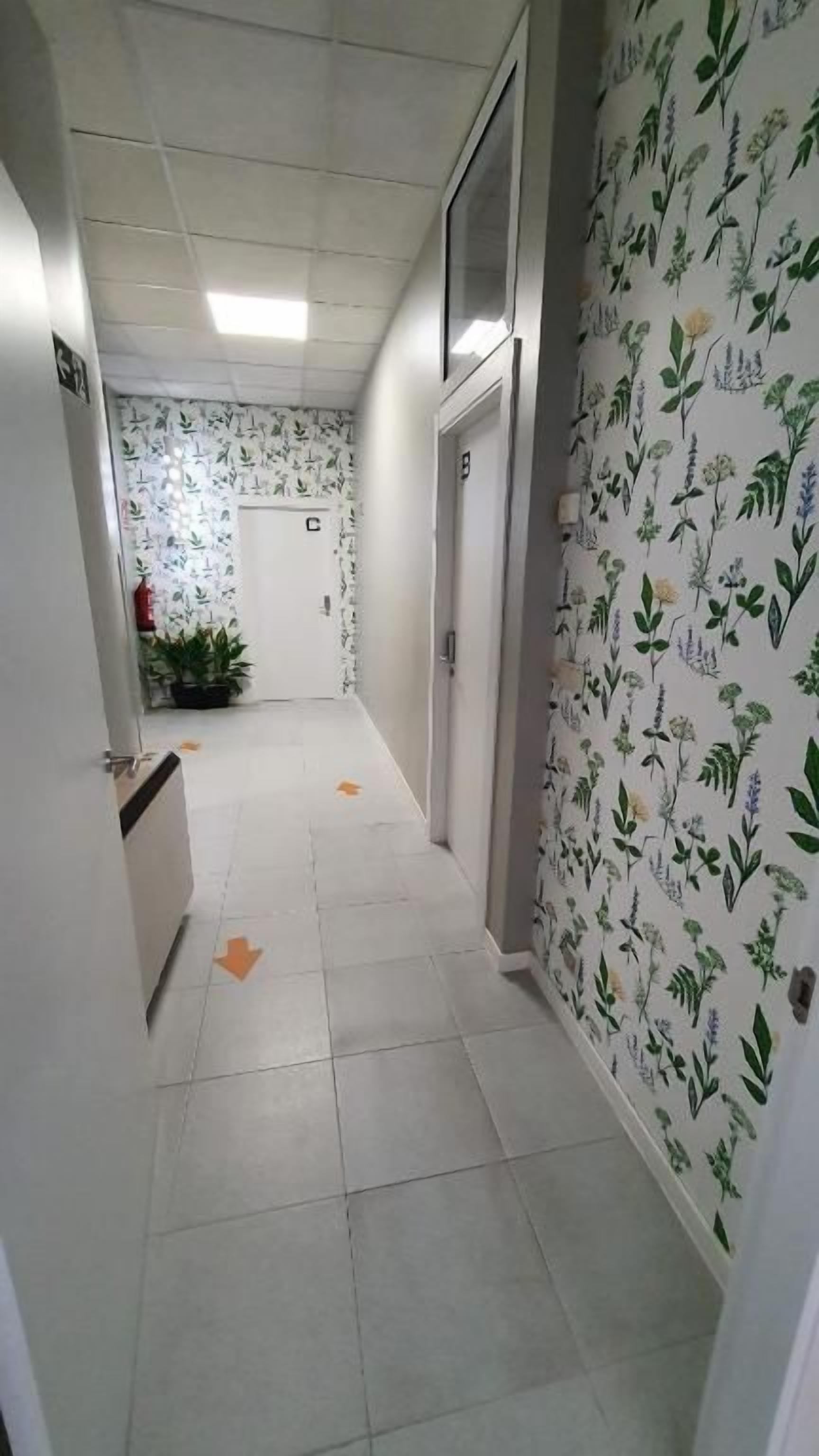 Een gang met een betegelde vloer, een deur met een letter en een wand met een bloemenmotief.