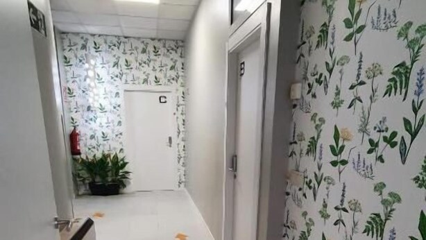 Un pasillo con suelo de baldosas, una puerta marcada con una letra y una pared con estampado floral.