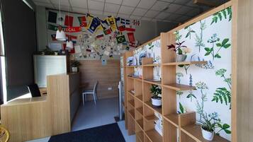 Een receptiezone met een houten bureau, een stoel en planken met potplanten. Vlaggen hangen aan de muur.