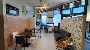 A modern cafe with wooden partitions, tables, chairs, a sofa, and a large window with a view. - Albergue Turistico la Credencial - Hostel (Santiago de Compostela)