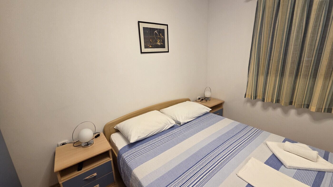 Habitación de hotel con una cama, mesitas de noche, una lámpara, un cuadro en la pared y una ventana con cortinas.