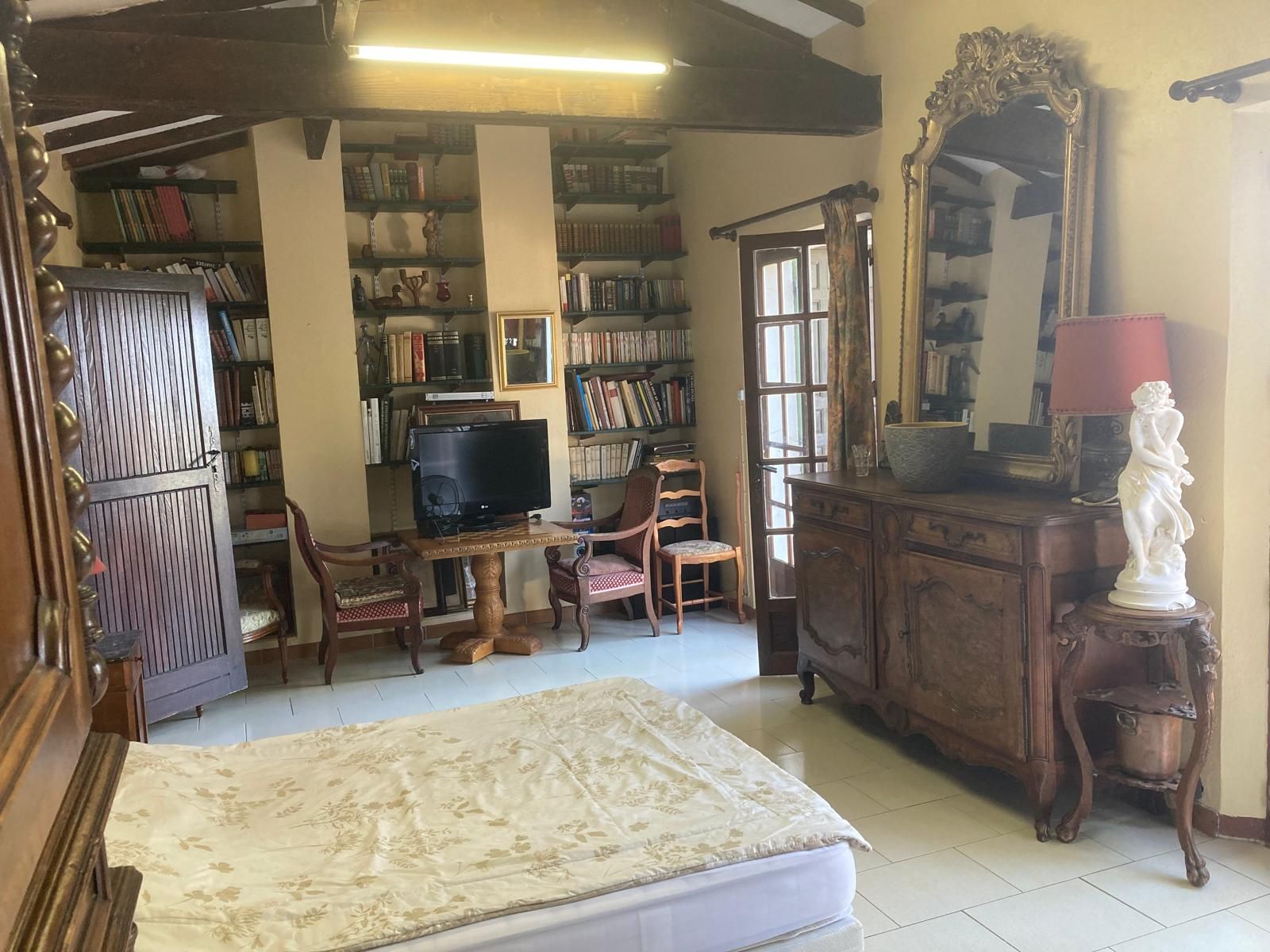 A room with a bed, a television, a bookshelf, a statue, and a mirror.