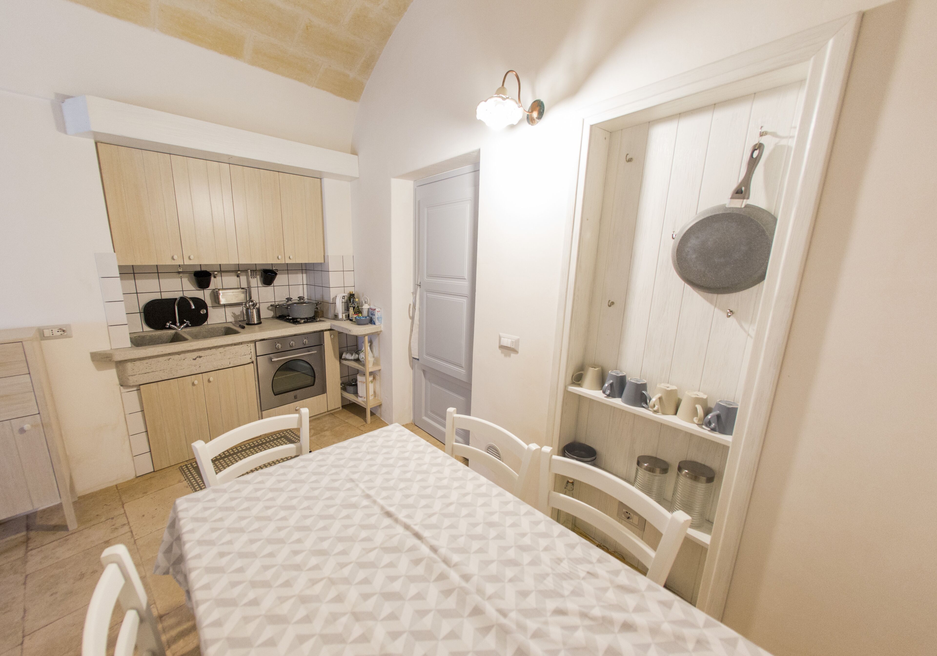 A compact kitchen with wooden cabinets, a dining table with chairs, and a hanging pot rack.