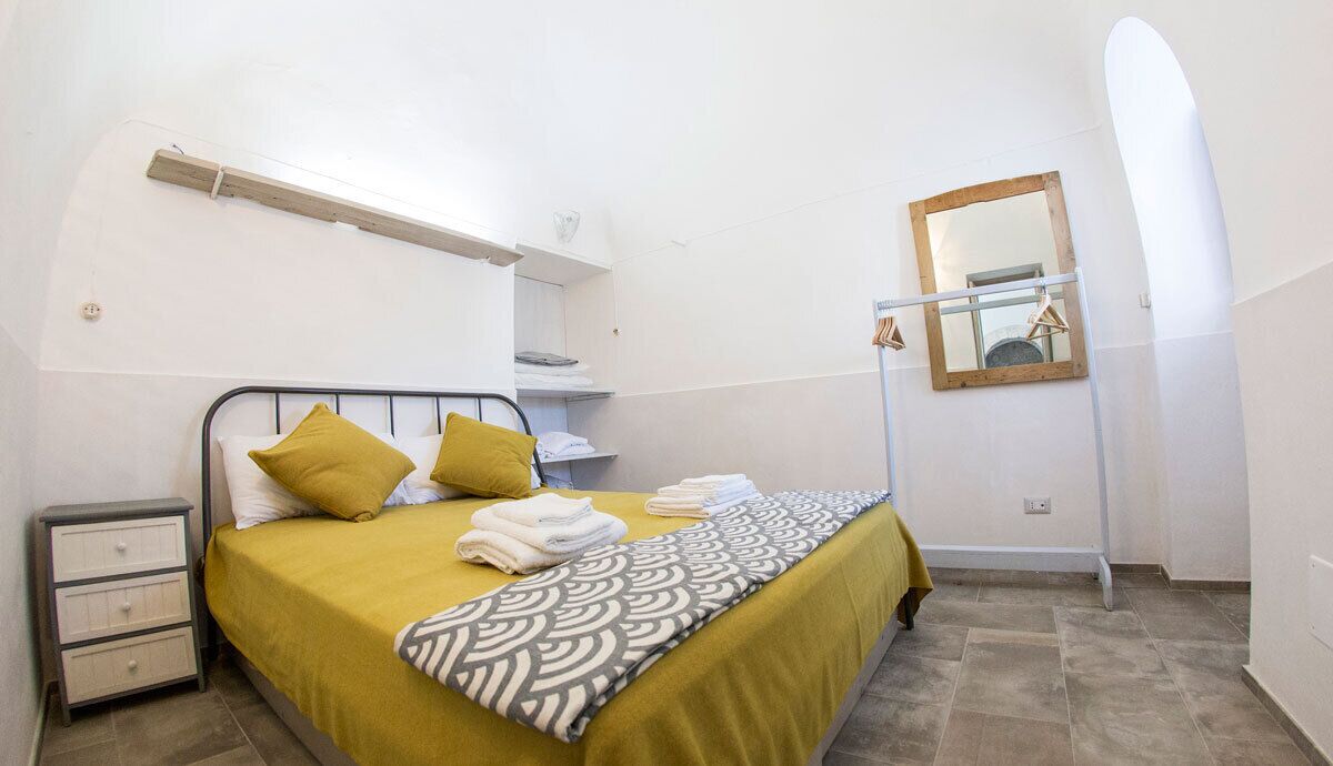 A bedroom with a bed, a bedside table, a mirror, and a towel rack.