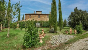 A stone building with a garden path, statues, and tall trees.