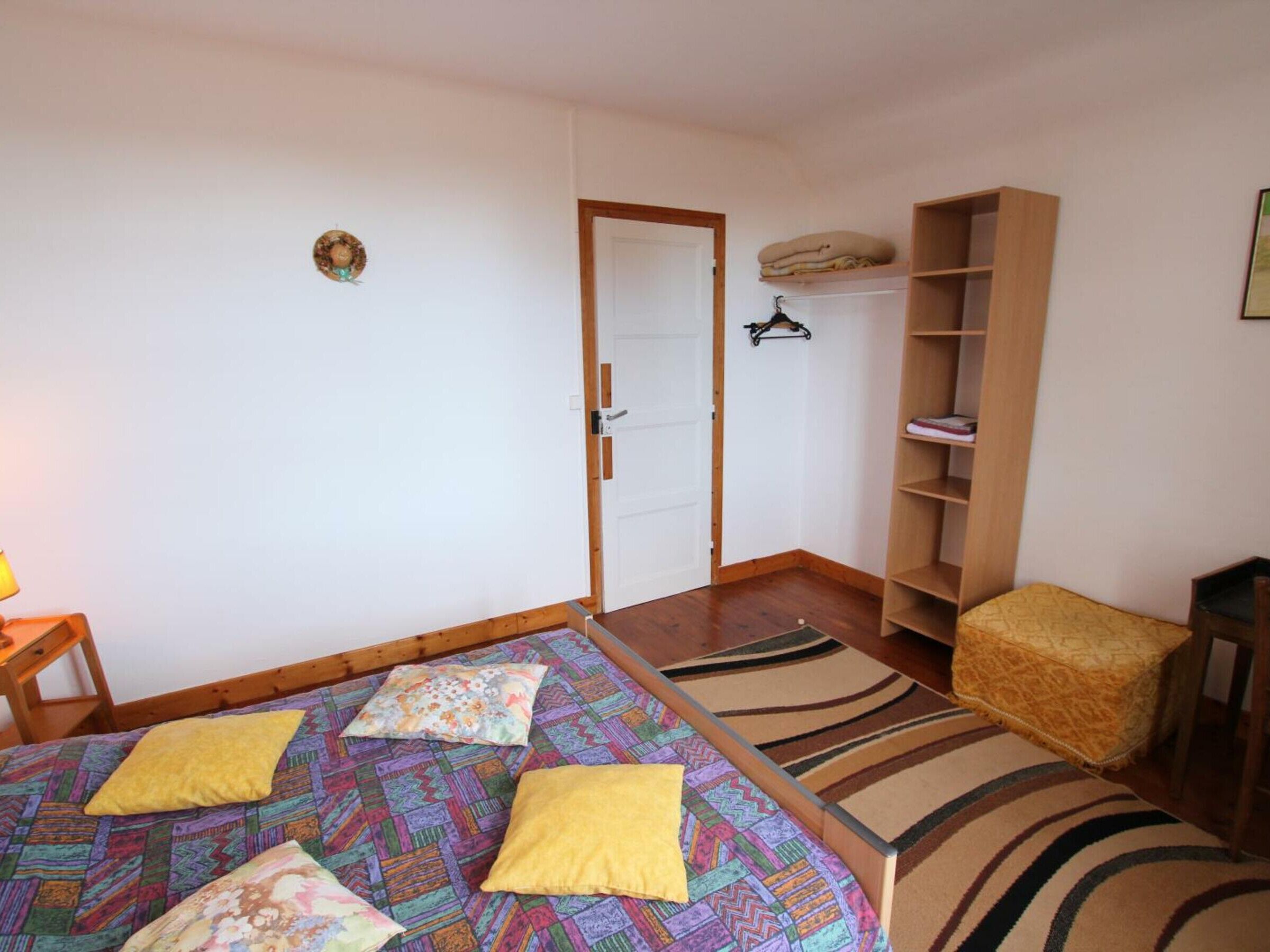 Ein Zimmer mit einem Bett, einem Sessel, einem Bücherregal und einer Tür.