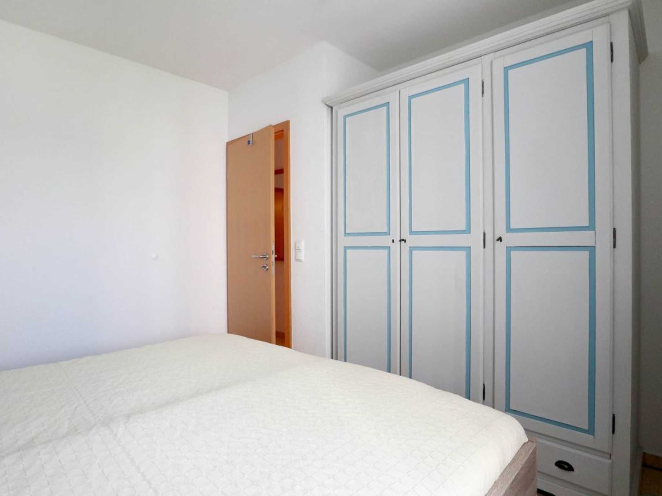 A bedroom with a bed, a wardrobe, and a door leading to another room.