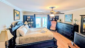 A bedroom with a large bed, a ceiling fan, a bookshelf, a chair, and a dresser.