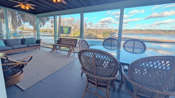 A covered outdoor seating area with a sofa, chairs, and a table, overlooking a body of water.