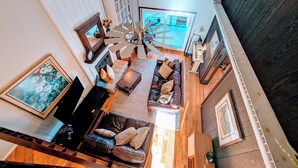 A spacious living area with a fireplace, a ceiling fan, and a large window overlooking a balcony.