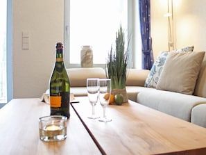 Une pièce avec une table en bois, une bouteille, deux verres, une bougie, un vase et une plante.
