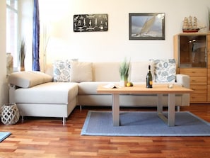 Ein Wohnzimmer mit einer Couch, einem Holztisch, einem Schiffsmodell, einem gerahmten Bild und maritimer Dekoration.