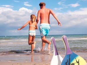 Une scène de plage avec deux personnes qui marchent en direction de l’eau, une planche de surf et un parasol de plage.