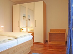 Een slaapkamer met een bed, een kledingkast, een nachtkastje en een klein houten bankje.