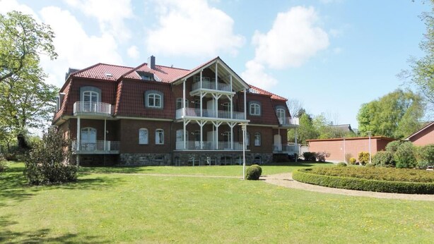 A large, two-story building with a red-tiled roof, a balcony on the second floor, and a well-maintained lawn in front. - Villa Seegarten Whg. Seg07 (Ostseebad Boltenhagen)
