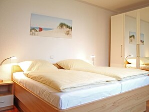 Un lit double avec une tête de lit en bois, deux tables de chevet avec des lampes, un tableau au mur et une armoire avec un miroir.