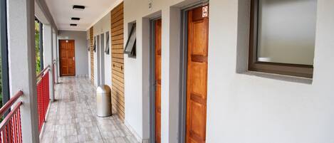 Un couloir avec des portes numérotées, une poubelle et une fenêtre sur le côté droit.