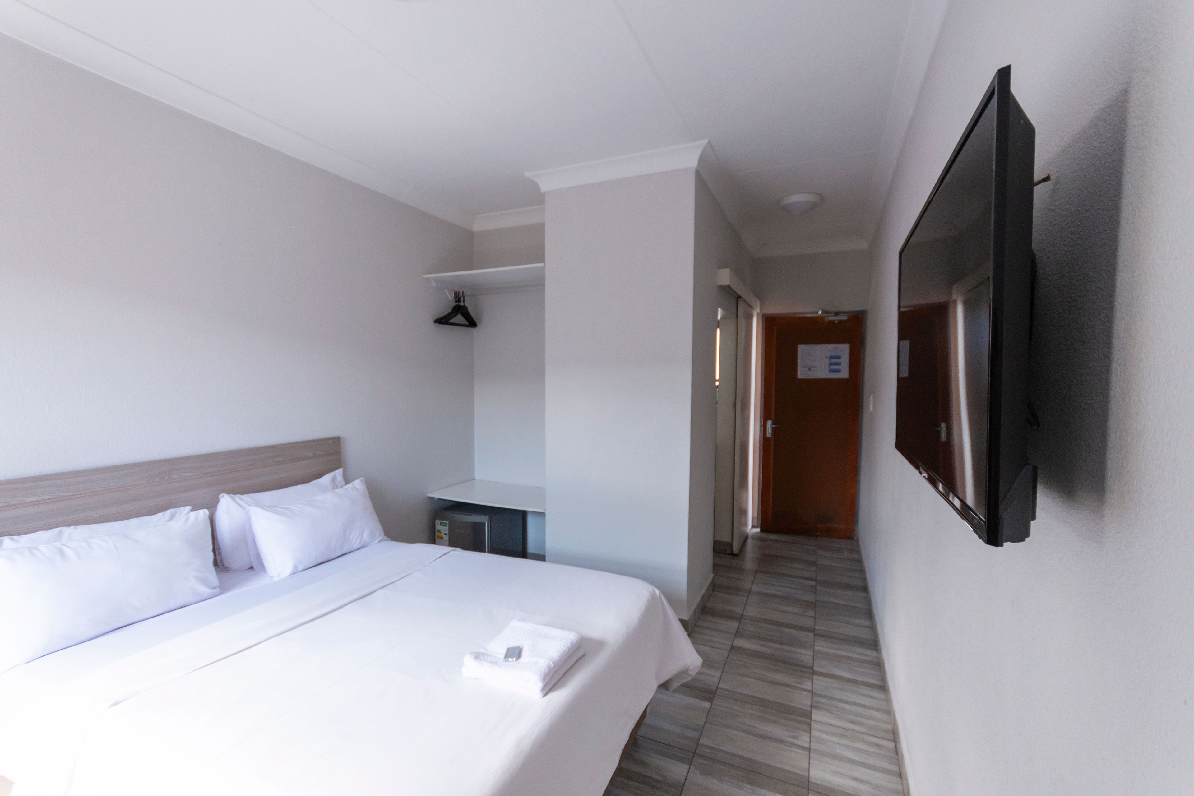 Een hotelkamer met een bed, een flatscreen televisie aan de muur, een kledingkast en een klein bureau.