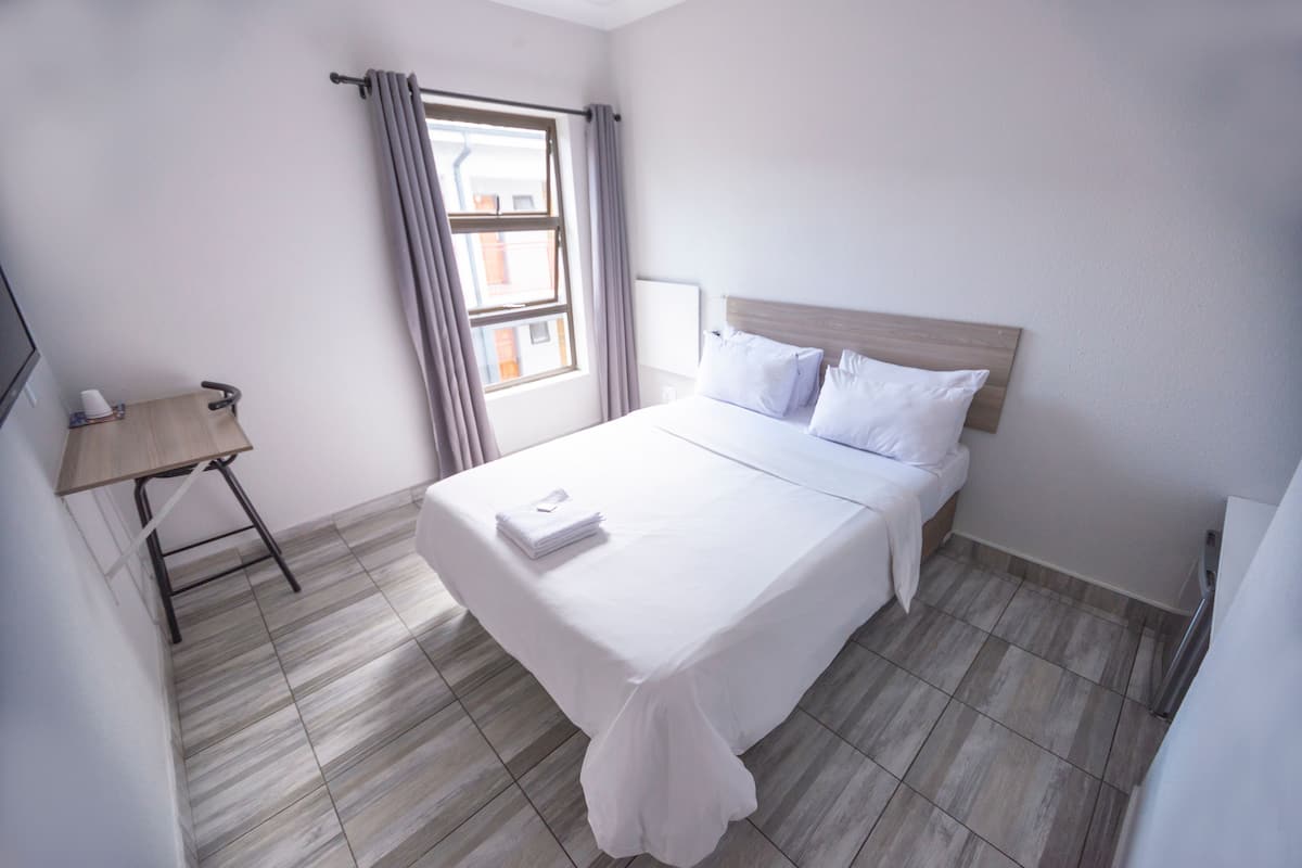 A neatly made bed with white linens, a wooden headboard, and a small table with a chair to the left.