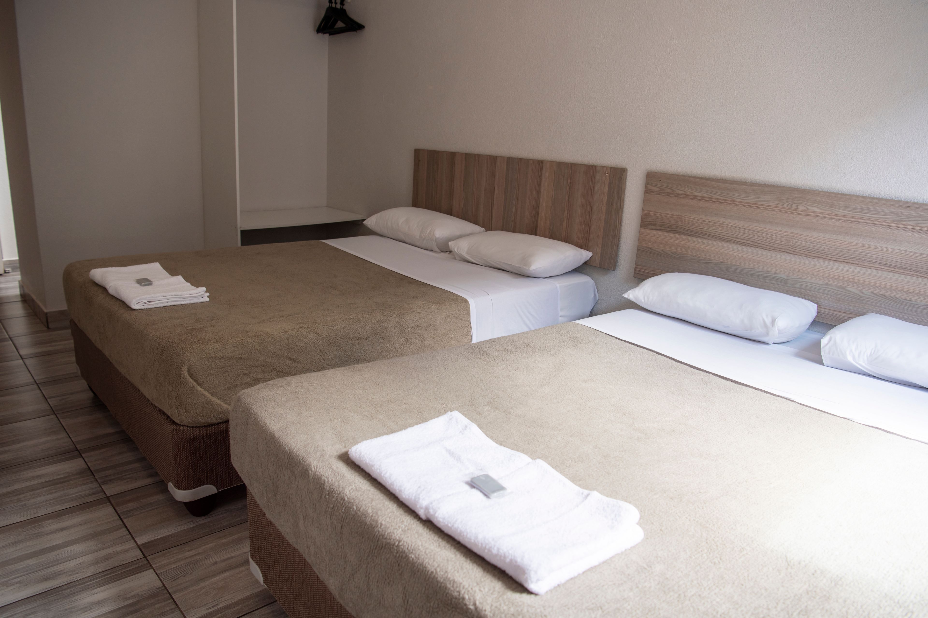 Habitación de hotel con dos camas, cada una con cabecero de madera, sábanas blancas y una toalla doblada sobre la cama.
