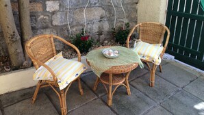 Two wicker chairs with striped cushions, a woven table, and a potted plant with red flowers.