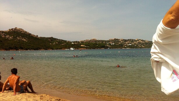 A beach with clear water, people swimming, and boats.