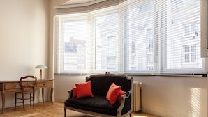 Una habitación con un sofá negro, cojines rojos, un escritorio de madera y una silla.