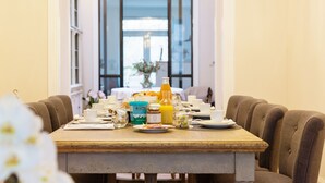 Una mesa de desayuno dispuesta con tazas, platos y diversas opciones para el desayuno, incluyendo una botella de jugo de naranja y un tarro de mermelada.