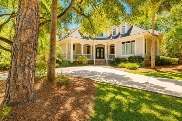 A two-story house with a front porch, a driveway, and surrounding trees.