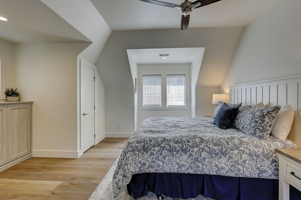A bedroom with a bed, a nightstand, a ceiling fan, and a window with blinds.
