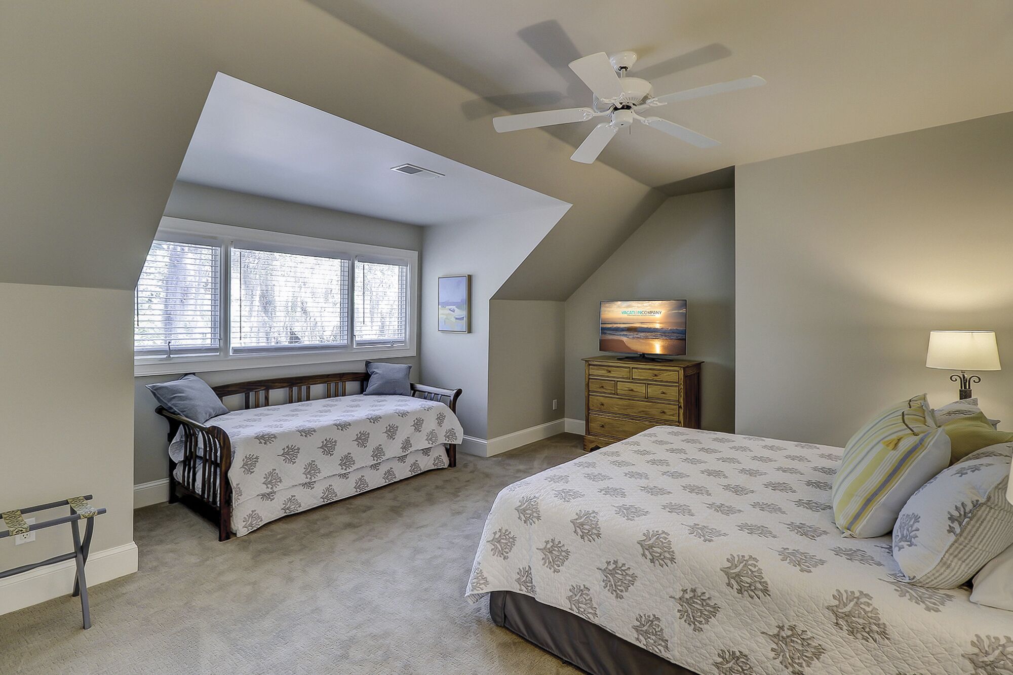 A bedroom with a sloped ceiling, two beds, a dresser, a TV, and a ceiling fan.