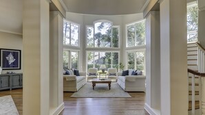 A spacious living room with a high ceiling, large bay windows, and hardwood flooring. - 13 Duck Hawk -Relax on the Front porch w/ rockers and a private pool! (Hilton Head Island)