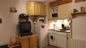 Eine kompakte Küche mit Holzausstattung, einer Waschmaschine, einer Mikrowelle und einem kleinen Fernseher auf einem Holzständer.