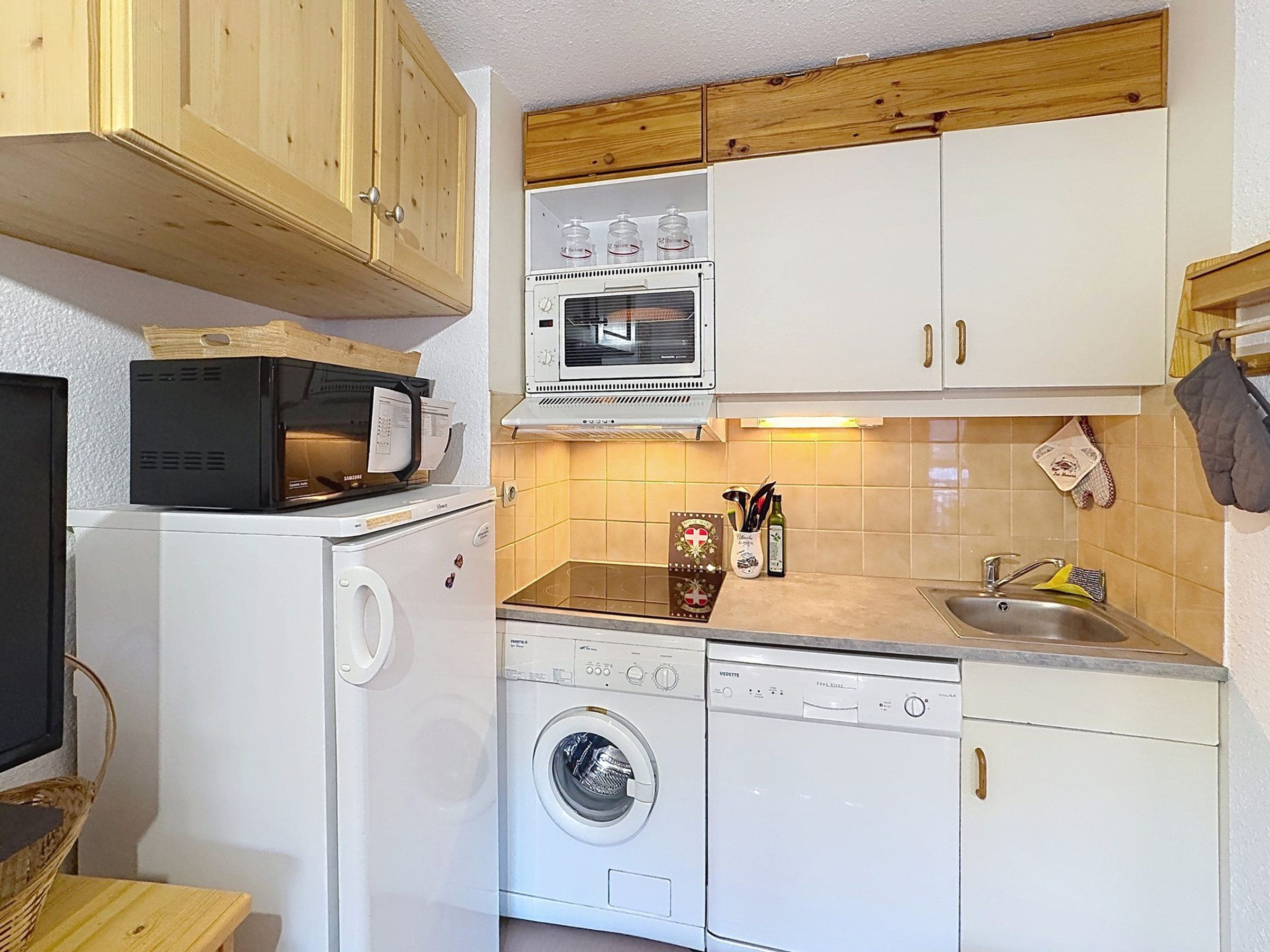 A compact kitchen with a microwave, oven, washing machine, and dishwasher.