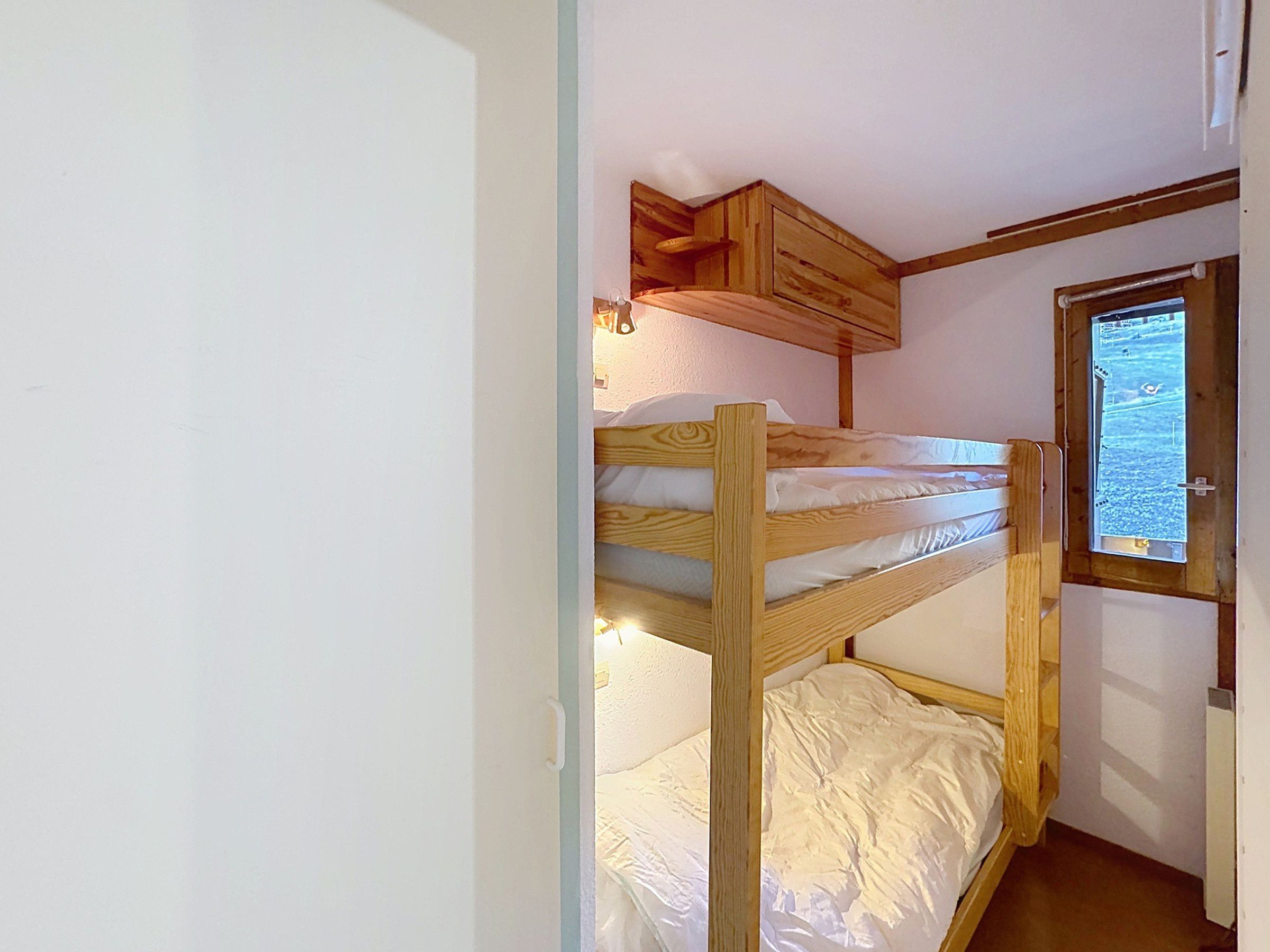 A bunk bed with a wooden headboard and a window with a view of a landscape.