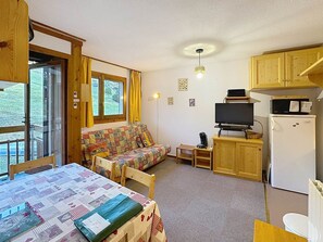 A cozy room with a sofa, a television, a refrigerator, and a dining table with a quilt.
