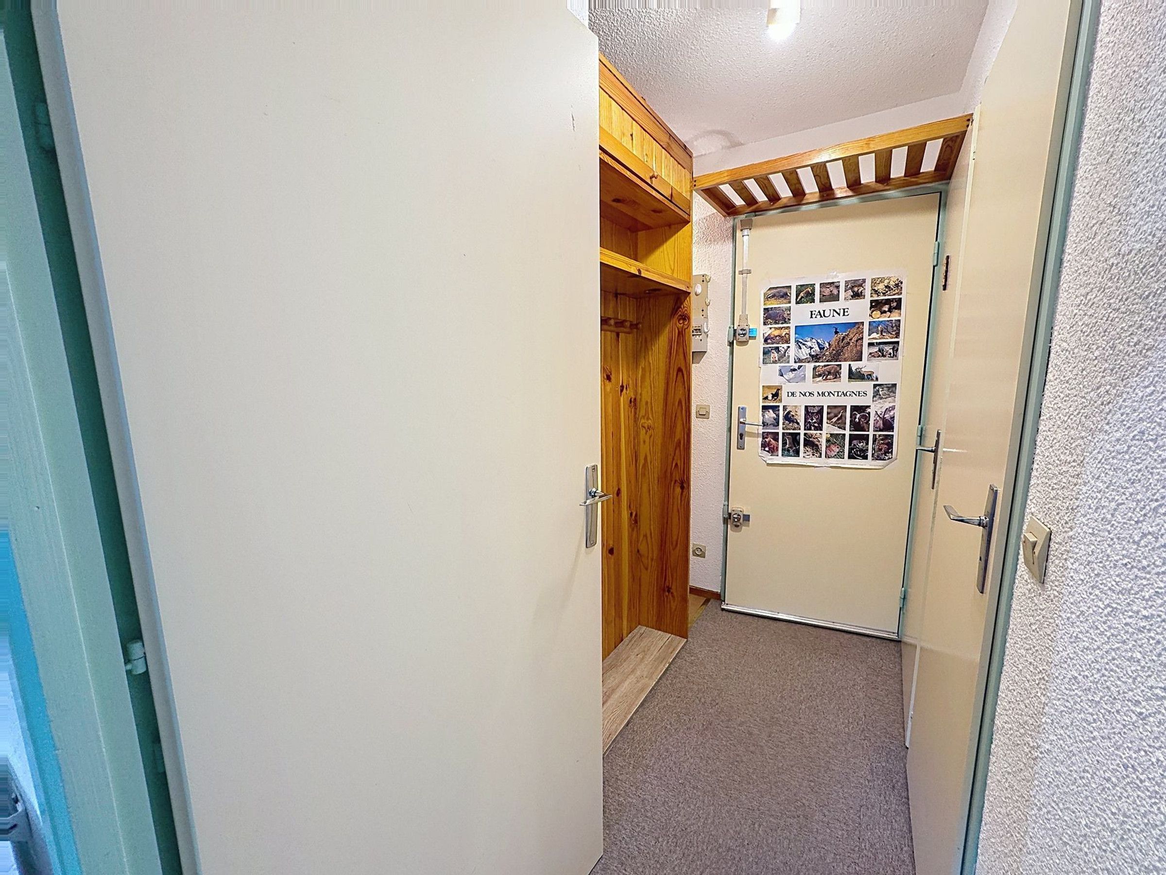 A narrow hallway with a wooden door and a poster on the wall.