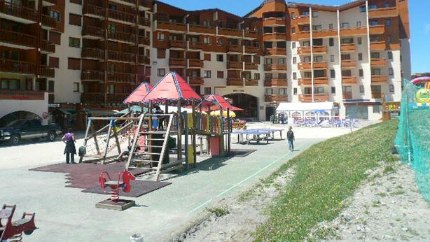 Ein Spielplatz mit Schaukeln und Rutschen, umgeben von mehrstöckigen Wohngebäuden.