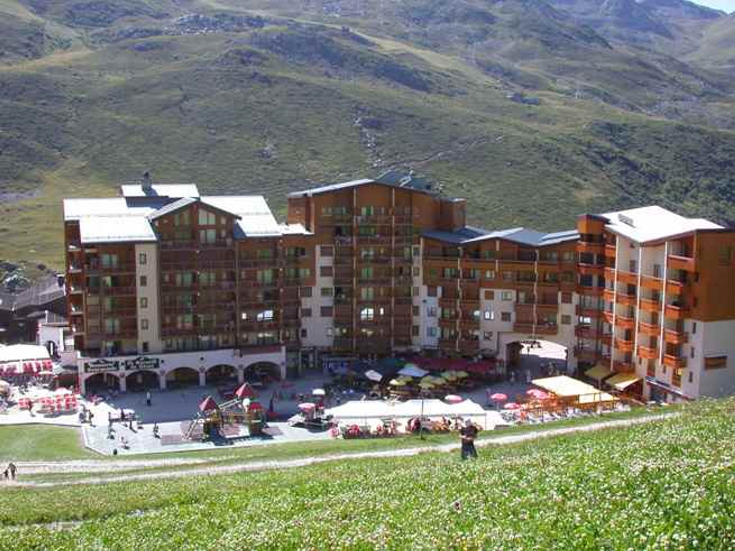 A multi-story hotel with balconies, a central courtyard with outdoor seating, and a mountainous backdrop.