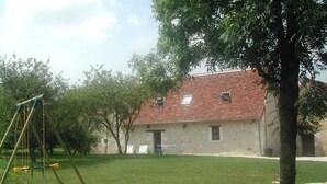 A grassy area with a swing set, a stone building with a tiled roof, and trees. - Charming 18th Century Gîte with Garden, Near Castles & Vineyards, Pet Friendly (Betz-le-Château)
