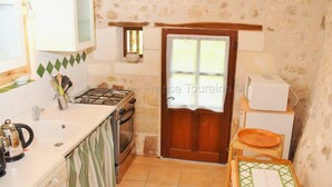 A compact kitchen with a stove, oven, and microwave. There's a wooden door with a window, and a small table with a cutting board. - Charming 18th Century Gîte with Garden, Near Castles & Vineyards, Pet Friendly (Betz-le-Château)